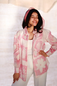 Woman wearing a pink floral cardigan over a white top and pants on a light background