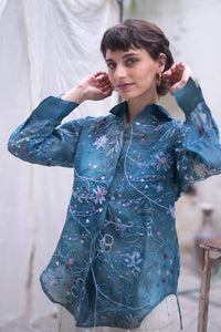 Woman wearing a blue floral patterned shirt, named as Blue Queen's Bagh, made by HeenaAgrima against a neutral background. 
