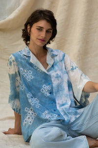 Woman wearing HeenaGrima's Butterfly Shirt, a light blue and white outfit with a floral pattern of shibori against a beige curtain background