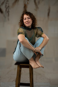 Woman sitting on a wooden stool against a plain background