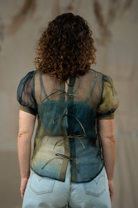 Person wearing a sheer top with a patterned design against a neutral background