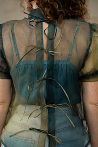 Person wearing a sheer green top with ribbons and a beige skirt.