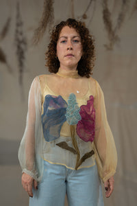 Woman wearing HennaAgrima's Clara Top a sheer top with floral appliqués against a neutral background