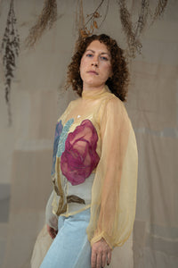 Woman wearing HennaAgrima's Clara Top a sheer top with floral appliqués against a neutral background