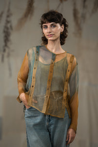 Woman wearing HeenaAgrima's Moss Organza Shirt, a sheer top with brown sleeves and blue jeans against a neutral background