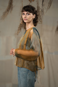 Woman wearing HeenaAgrima's Moss Organza Shirt, a sheer top with brown sleeves and blue jeans against a neutral background
