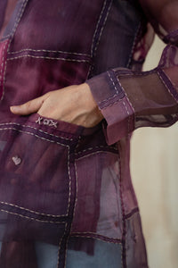 Close-up of a hand of a Woman wearing HeenaAgrima's Purple Dream Silk Organza Jacket, a sheer purple jacket over a dark top with light blue jeans against a neutral background