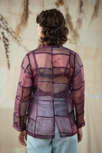 Back of a Woman wearing HeenaAgrima's Purple Dream Silk Organza Jacket, a sheer purple jacket over a dark top with light blue jeans against a neutral background
