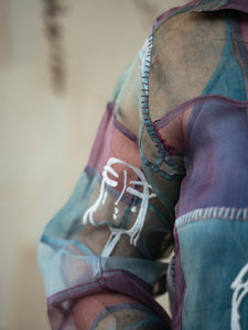 Close-up of the hand of a Woman wearing Stormy 2.0 patchwork shirt a colorful, patterned shirt with a neutral background