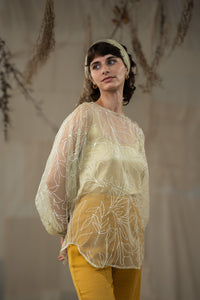 Woman wearing HeenaAgrima's Yellow Eve Silk Organza Top, a sheer top with leaf patterns and yellow pants against a neutral background