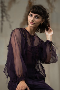 Woman wearing HeenaAgrima's Aubergine Zoe Silk Organza Top, a sheer purple blouse with ruffled details against a neutral background.