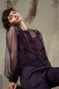 Woman wearing HeenaAgrima's Aubergine Zoe Silk Organza Top, a sheer purple blouse with ruffled details against a neutral background. 