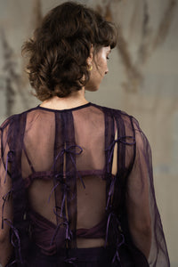 Woman wearing HeenaAgrima's Aubergine Zoe Silk Organza Top, a sheer purple blouse with ruffled details against a neutral background. 