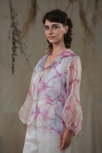 Woman wearing HeenaAgrima's pink quartz shirt, a pastel tie-dye pink shirt with a blurred background