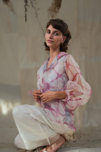 Woman wearing HeenaAgrima's pink quartz shirt, a pastel tie-dye pink shirt with a blurred background