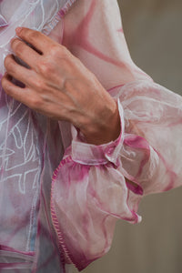 Close-up of the hand of the Woman wearing HeenaAgrima's pink quartz shirt, a pastel tie-dye pink shirt with a blurred background