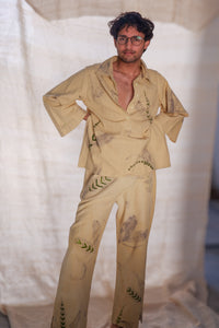 Man wearing a beige embroidered outfit against a white curtain background