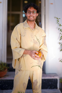 Person wearing a light yellow traditional outfit with intricate patterns, standing outdoors.