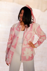 Woman wearing a pink floral jacket and white pants against a plain background