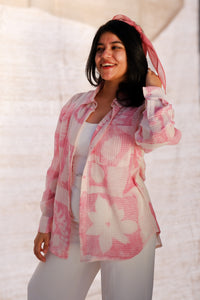 Woman wearing a pink floral shirt and white pants against a light background