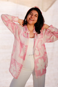Woman wearing a pink floral blouse over a white top and pants on a plain background
