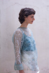 Woman wearing a sheer top with floral patterns against a plain background - HeenaAgrima
