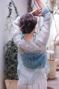 woman wearing a sheer white top named as tinsel top by HeenaAgrima with blue accents in an outdoor setting