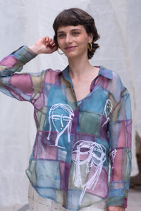 Woman wearing a HeenaAgrima's colorful sheer shirt with abstract designs against a neutral background