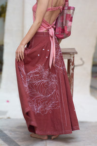 Woman wearing a pink top and maroon skirt with floral white patterns, designed by HeenaAgrima, named as red Valen Skirt, holding a plaid bag.