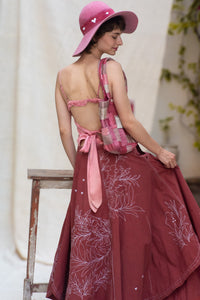 Woman wearing a pink top and maroon skirt with floral white patterns, designed by HeenaAgrima, named as red Valen Skirt, holding a plaid bag.