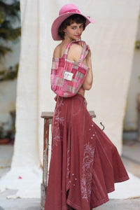 Woman wearing a pink top and maroon skirt with floral white patterns, designed by HeenaAgrima, named as red Valen Skirt, holding a plaid bag.