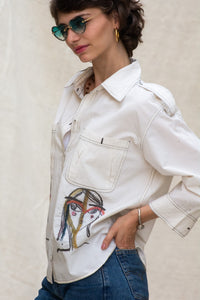 Woman wearing heeenaAgrima's Nina Cotton Shirt a white shirt with colorful face designs, holding sunglasses.