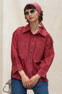 Woman wearing a red organic cotton shirt, named cherry, made by HeenaAgrima and pink headscarf against a plain background. 