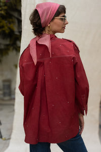 Woman wearing a red organic cotton shirt, named cherry, made by HeenaAgrima and pink headscarf against a plain background. 