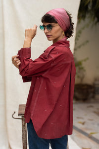 Woman wearing a red organic cotton shirt, named cherry, made by HeenaAgrima and pink headscarf against a plain background. 