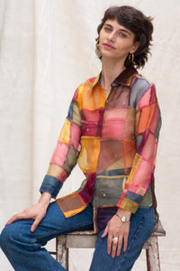 Woman wearing HeenaAGrima's OG Indradhanush Shirt, a colorful patchwork shirt sitting on a stool against a white background