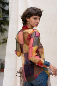 Woman wearing HeenaAGrima's OG Indradhanush Shirt, a colorful patchwork shirt against a white blurred background. 