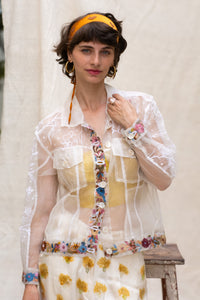 Woman wearing a floral white jacket, made in organza, named bloom 2.0 by designers HeenaAgrima with a sheer overlay against a neutral background