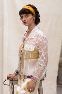 Woman posing one side and wearing a floral white jacket, made in organza, named bloom 2.0 by designers HeenaAgrima with a sheer overlay against a neutral background