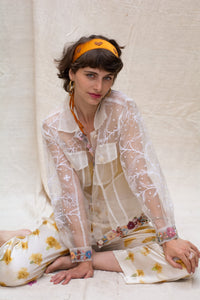 Woman wearing a floral white jacket, made in organza, named bloom 2.0 by designers HeenaAgrima with a sheer overlay against a neutral background