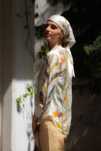 Woman wearing a floral shirt, named Garden Shirt by HeenaAgrima standing against a textured wall.