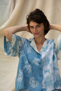 Woman wearing HeenaGrima's Butterfly Shirt, a light blue and white outfit with a floral pattern of shibori against a beige curtain background