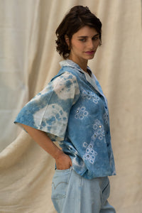 Woman wearing HeenaGrima's Butterfly Shirt, a light blue and white outfit with a floral pattern of shibori against a beige curtain background