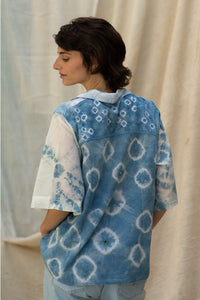 Woman wearing HeenaGrima's Butterfly Shirt, a light blue and white outfit with a floral pattern of shibori against a beige curtain background