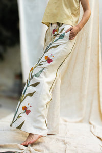 A Woman wearing HeenaAgrima's Garden pants, white pants with floral patterns, standing against a neutral background.