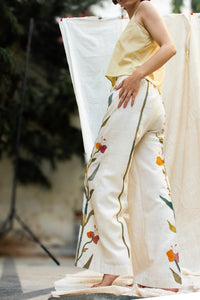 Close-up of a Woman wearing HeenaAgrima's Garden pants, white pants with floral patterns, standing against a neutral background.