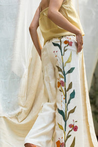 Close-up of a Woman wearing HeenaAgrima's Garden pants, white pants with floral patterns, standing against a neutral background.