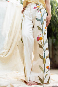 Close-up of a Woman wearing HeenaAgrima's Garden pants, white pants with floral patterns, standing against a neutral background.