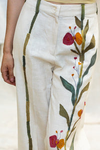 Close-up of a Woman wearing HeenaAgrima's Garden pants, white pants with floral patterns, standing against a neutral background.