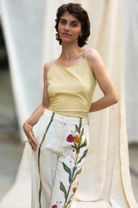 A Woman wearing HeenaAgrima's Garden pants, white pants with floral patterns, standing against a neutral background.